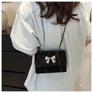 Detail of a black crossbody bag featuring a silver bow and elegant chain strap on a model