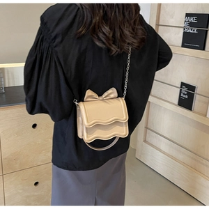 Detail view of beige crossbody bag with a large bow and wavy flap on a chain strap