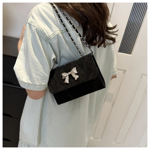 Detail of a black glossy leather crossbody bag with a silver metallic bow buckle