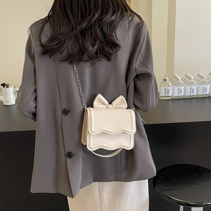 Chic beige chain crossbody bag with bow detail and wavy trim shown on a model