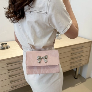 Pink mini crossbody bag with silver bow accent and metal chain strap on model