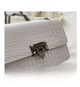Close-up of light grey faux crocodile skin bag with dark metal clasp and rivet details