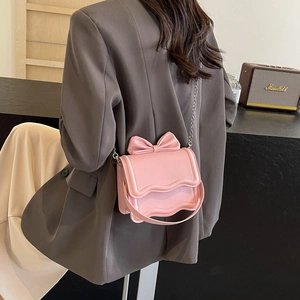 Pink crossbody bag with large bow and chain strap shown on a person wearing a grey blazer