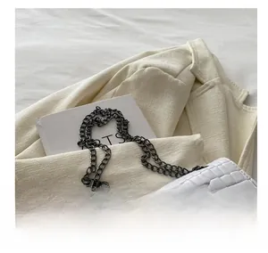 Close-up of white crocodile pattern leather bag with dark grey metal chain and buckle
