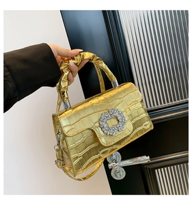 Detail of gold crocodile-patterned handbag with crystal buckle and ruched handle