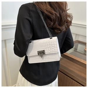 Detail of white crocodile embossed flap bag with dark metal chain strap on model