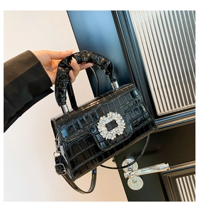 Detail of black crocodile texture handbag featuring a crystal buckle and ruffled handle