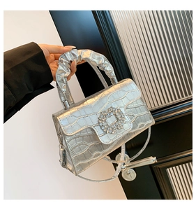 Close-up of silver crocodile embossed handbag with crystal buckle and ruched handle