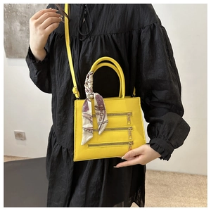 Detail of yellow PU crossbody bag with gold zippers and silk scarf on round handle