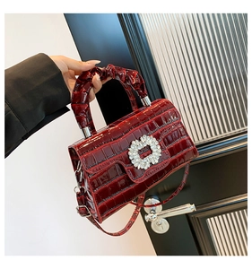 Detail of burgundy crocodile-embossed leather bag with sparkling crystal buckle and pleats