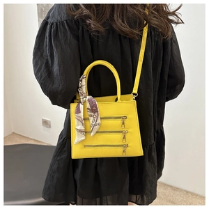 Detail of yellow crossbody bag with metal zippers and silk scarf on a black dress