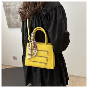 Detail view of yellow crossbody bag with triple zippers and silk scarf on handle