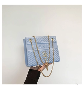 Détail d'un sac bandoulière matelassé bleu clair avec chaîne dorée et coutures en V