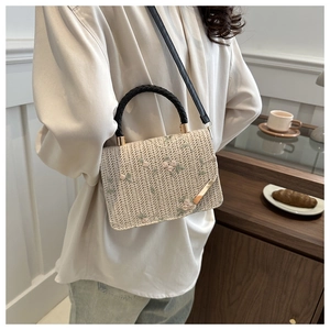 Détail du sac bandoulière en paille beige avec broderie florale rose et anse tressée noire