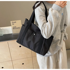 Dettaglio di una grande borsa tote in nylon nero con bottone a pressione e ampi spallacci