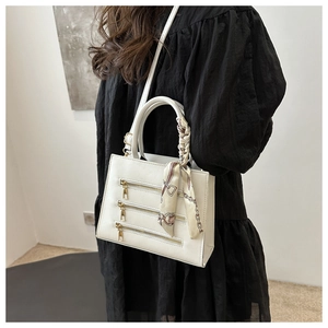 Close-up of white leather handbag with gold zippers and printed silk scarf on handle