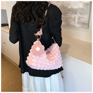 Detail of pink popcorn textured shoulder bag with floral charm worn on a shoulder