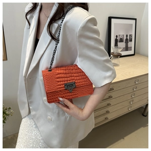 Detail of vibrant orange croc-embossed chain bag on model with metallic square clasp