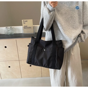 Vista laterale di una borsa tote in nylon nero capiente con tasche laterali su modella