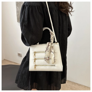 White PU leather crossbody bag with triple gold zippers and decorative silk scarf on handle