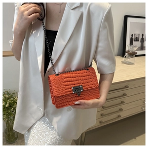 Detail of bright orange crocodile texture crossbody bag with metal chain strap on model