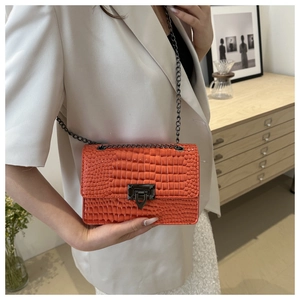 Detail view of bright orange crossbody bag with crocodile texture and metal chain strap