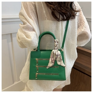 Detail of vibrant green tote bag with gold zippers and decorative silk scarf on handle