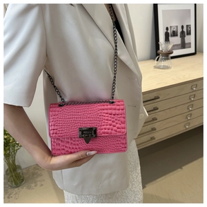 Pink crocodile texture crossbody bag with dark chain strap shown on a model