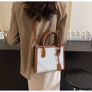 Détail d'un sac cabas à paillettes argentées avec lanières en cuir marron porté par un mannequin