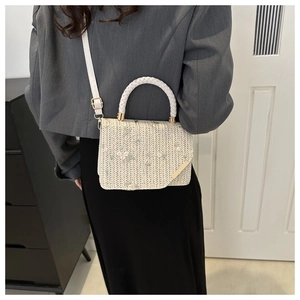 Détails de broderie sur sac à main en paille crème porté par un mannequin en intérieur