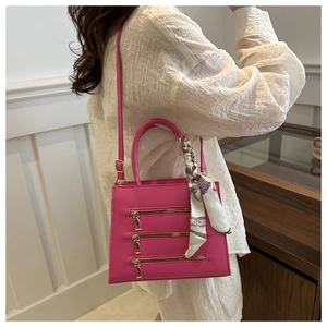 Detail of fuchsia crossbody bag featuring triple gold zippers and decorative silk scarf