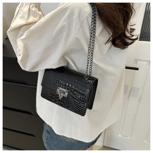 Detail of black faux-croc leather crossbody bag with silver buckle and chain strap