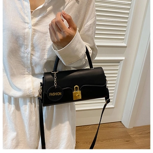 Detail of black minimalist underarm bag featuring a gold clasp and a fashion tag