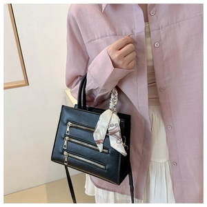 Chic black tote bag with gold zipper accents and silk scarf handle detail worn by model