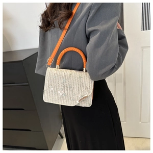 Gros plan du sac en paille tressée crème avec broderie florale et bandoulière en cuir orange