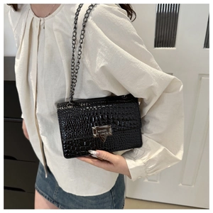 Detail of black faux leather crossbody bag with crocodile pattern and heart lock