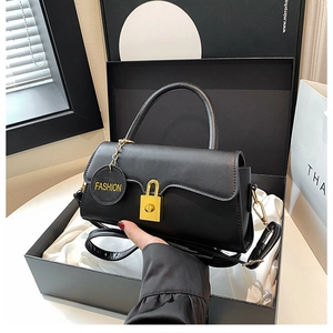 Detailed shot of black leather underarm bag with gold lock and round fashion tag in a gift box