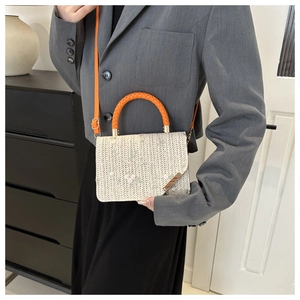 Détail d'un sac en paille avec broderie florale rose et poignées rondes orange