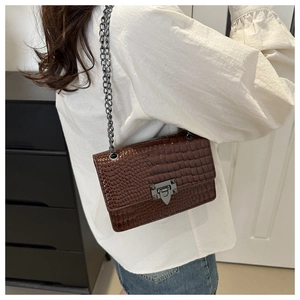 Detail of brown crocodile embossed shoulder bag with metallic lock on a casual outfit