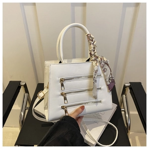 Detail view of white trapezoid tote bag with three decorative zippers and silk scarf handle