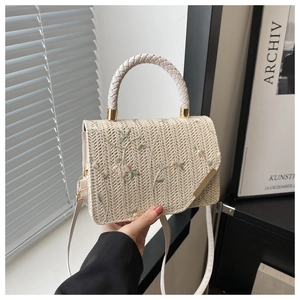 Détail d'un sac à main en paille beige avec broderie florale et poignée tressée
