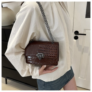 Side view of dark brown croc-embossed flap bag with dark grey chain strap on a model