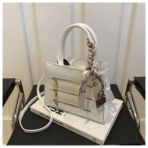 Detailed close-up of white leather handbag with gold zippers and decorative silk scarf wrap