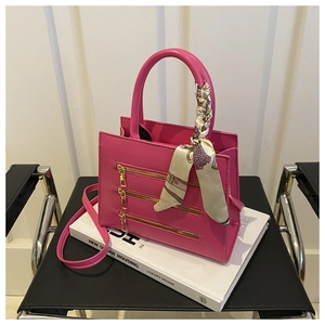 Detail of fuchsia leather crossbody bag with gold zippers and a silk scarf on the handle