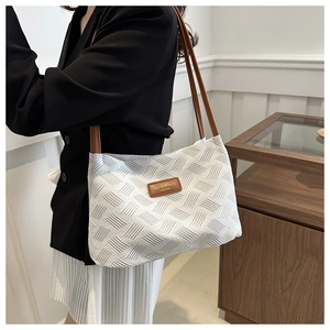 Detail of white quilted tote bag with brown leather straps and fashion label on shoulder