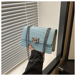 Close-up of light blue crocodile embossed square bag with metallic chain and buckle