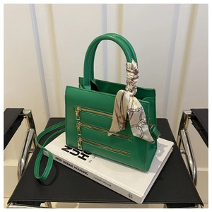 Detail of green crossbody bag with gold zippers and decorative silk scarf handle