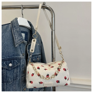 Detail der weißen Cord-Pilllow-Bag mit Erdbeer-Stickerei und goldener Blumen-Kette