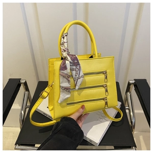 Close-up of bright yellow handbag with triple decorative zippers and floral silk scarf