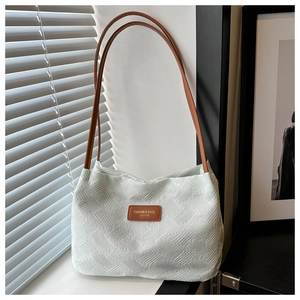 Close-up of textured woven fabric and leather logo tag on a large shoulder tote bag